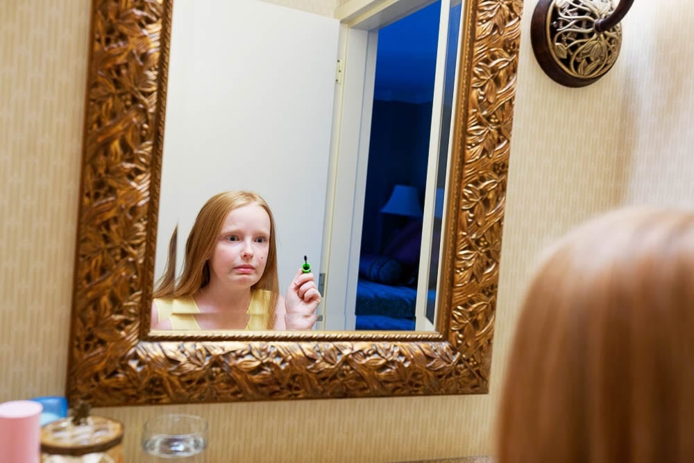 candid shot of flower girl make up in front mirror