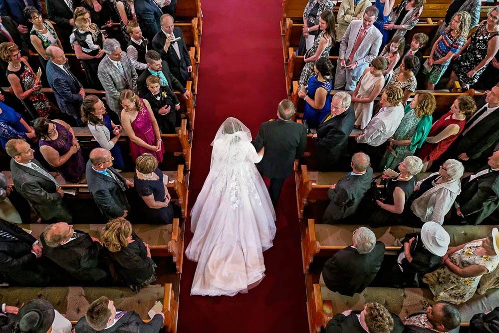 photo from balcony of bride and father of the bride walking down church aisle