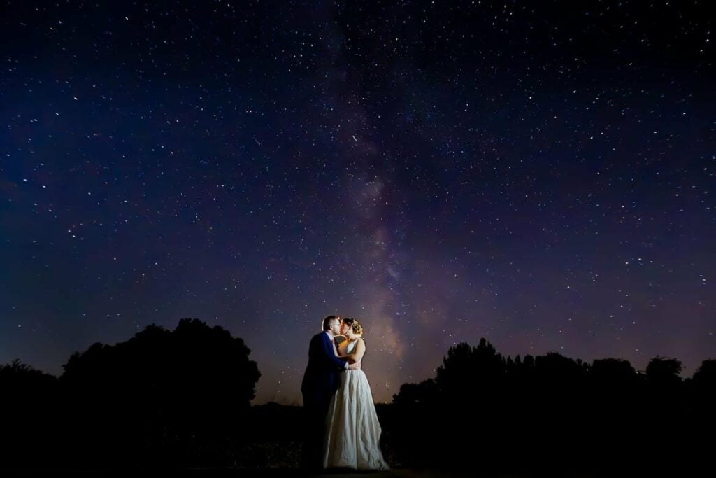 bride and groom kissing under milkyway