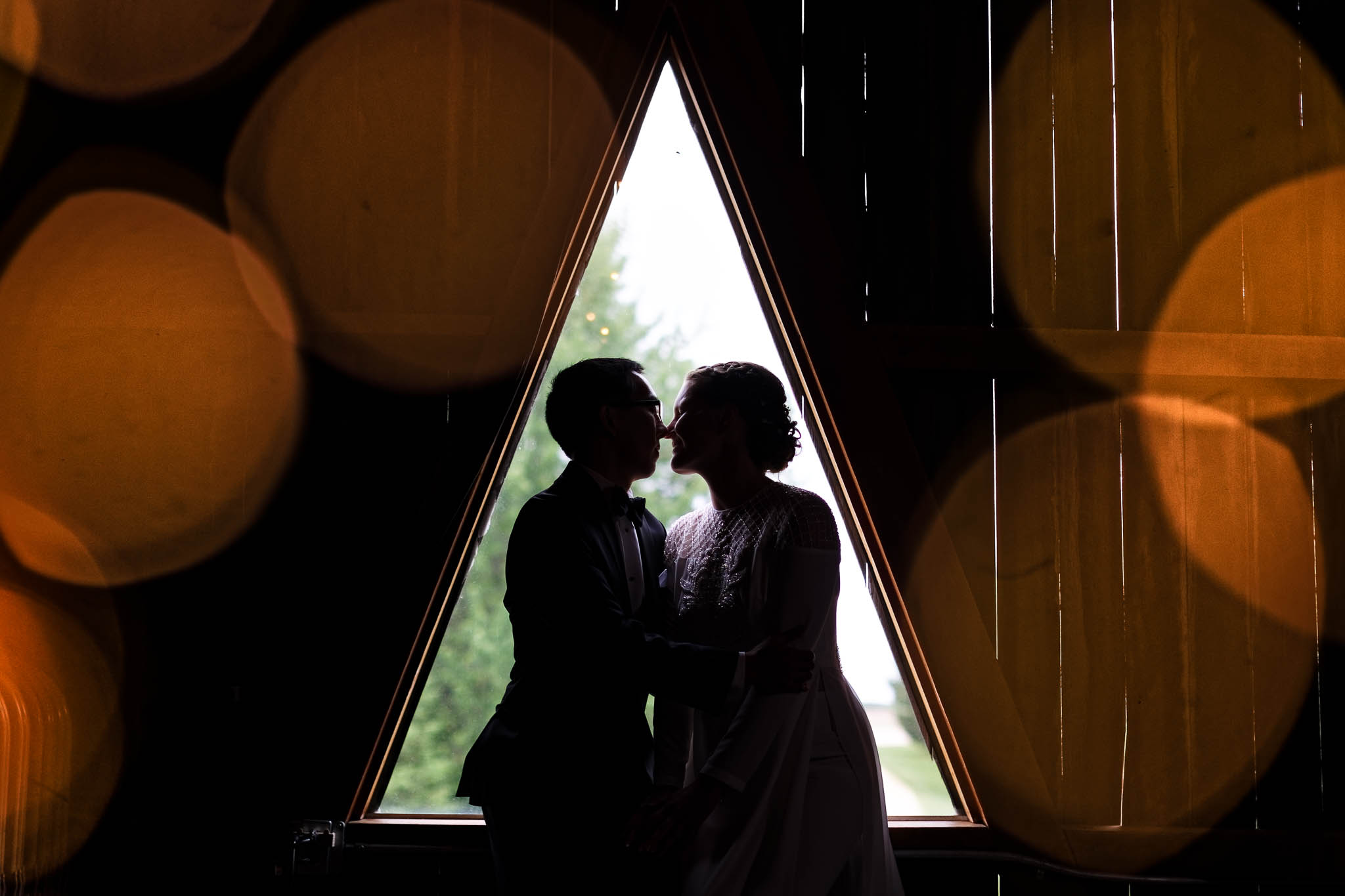 artistic silhouette of the bride and groom with the triangular windows at the top of the pond view barn