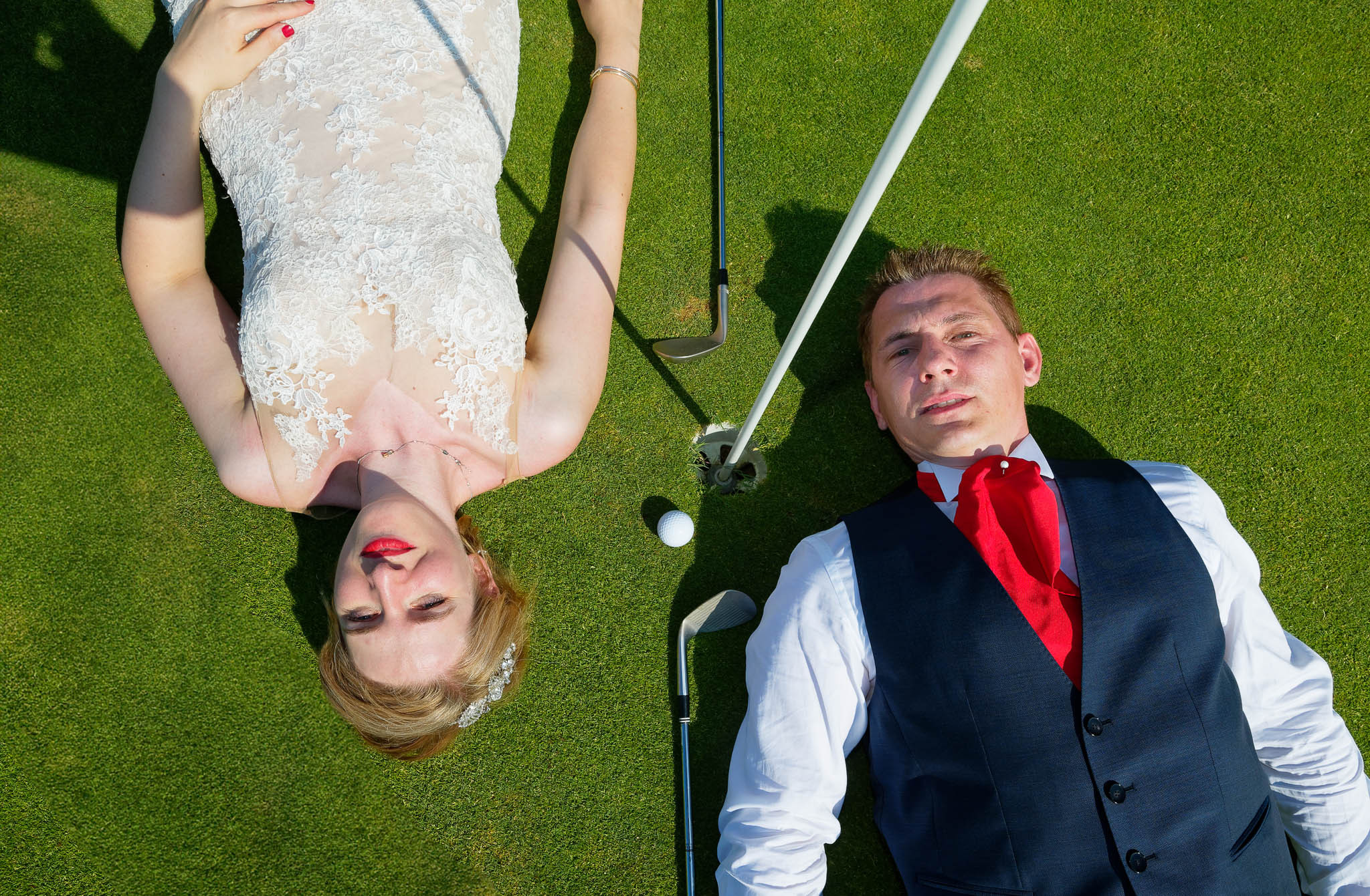 bride and groom lyaing on green golf course