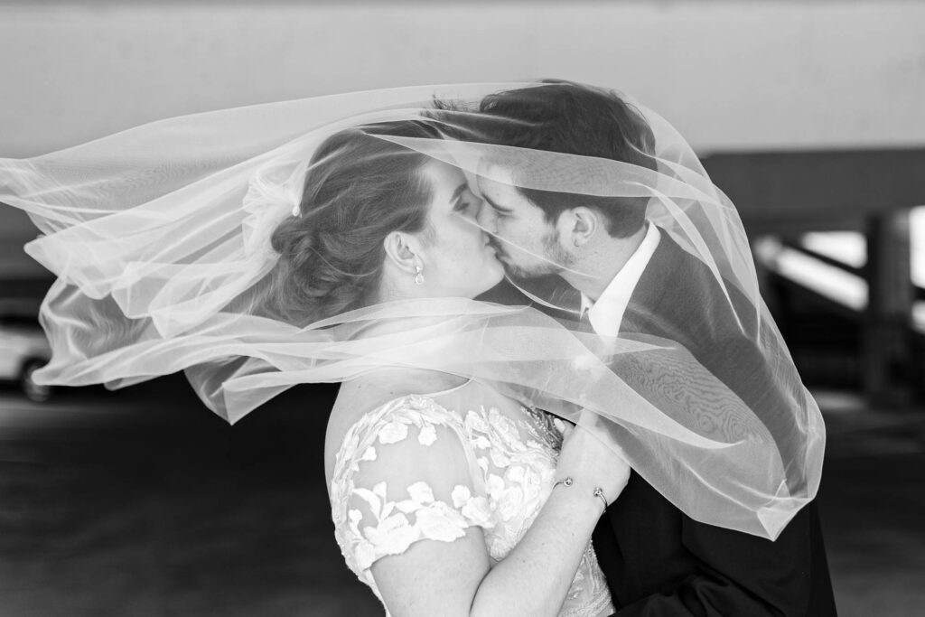 Black and white photo of married couple kissing under the veil