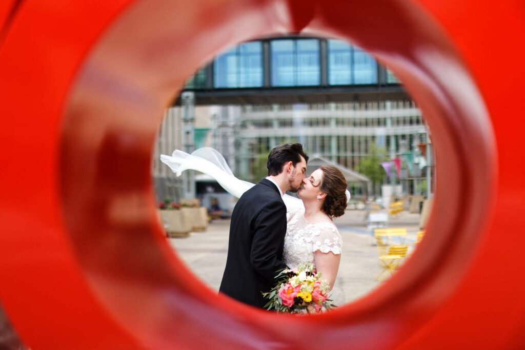Bride and groom, kissing with flying veil, though Rochester sign