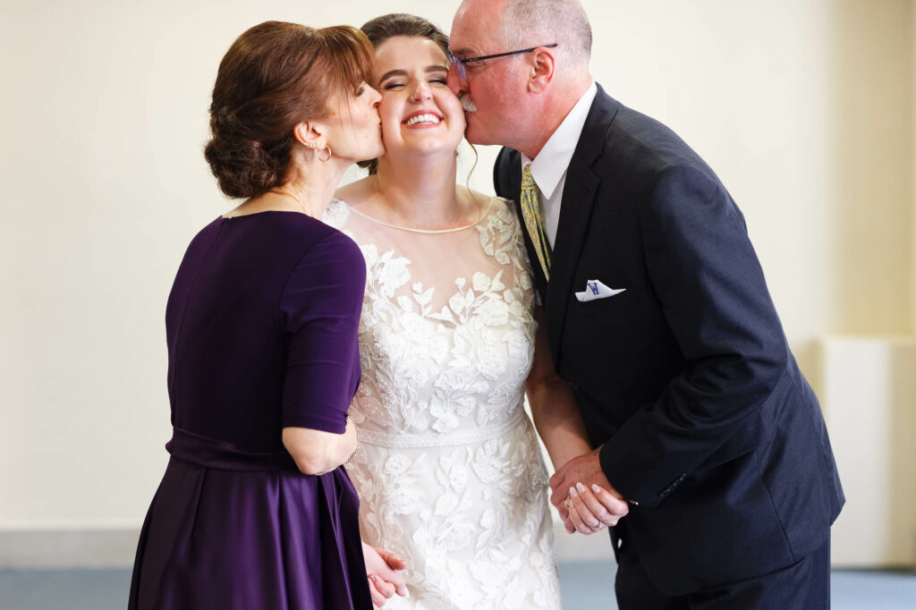Funny, first look of the bride with her parents, kissing her on the cheek