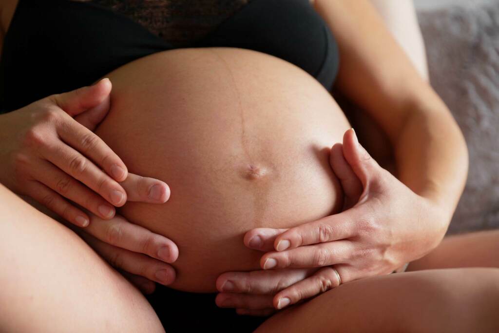 Intimate in-home pregnancy lifestyle photography in Rochester Minnesota showing a close-up of parents' hands on a maternity belly bump.