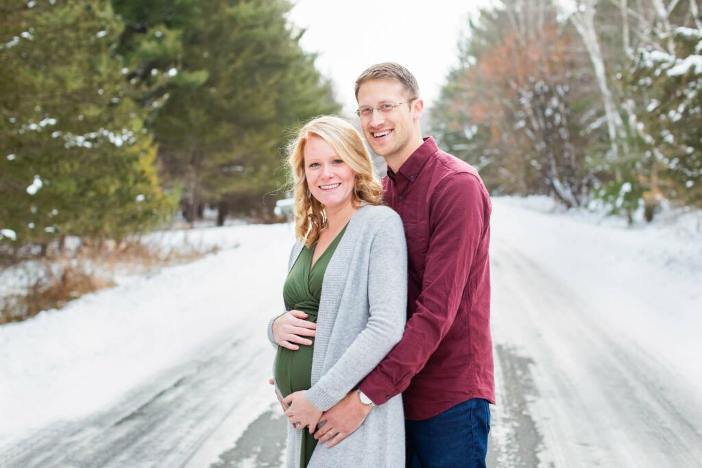 Winter maternity photo shoot in Rochester MN with a pregnant mother in a green dress surrounded by a snowy Minnesota pine forest.