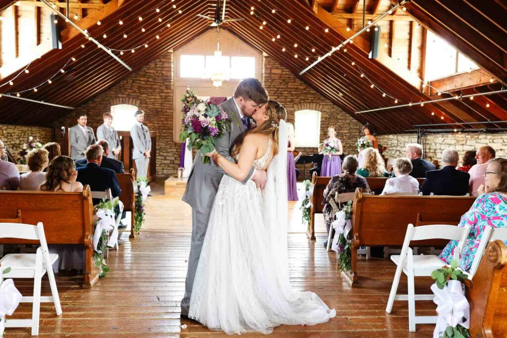 033-Married Couple kissing in the aisle at Wedding ceremony at the loft at Mayowood stone barn_
