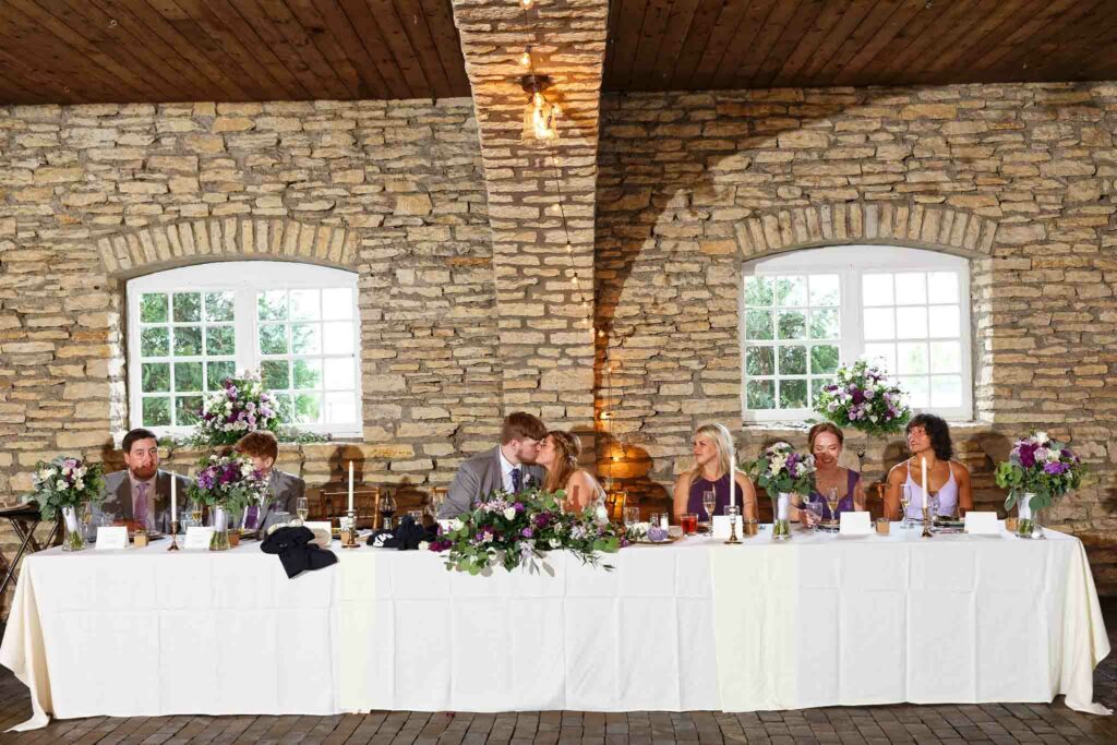 057-bride and groom kissing while guest tapping glass