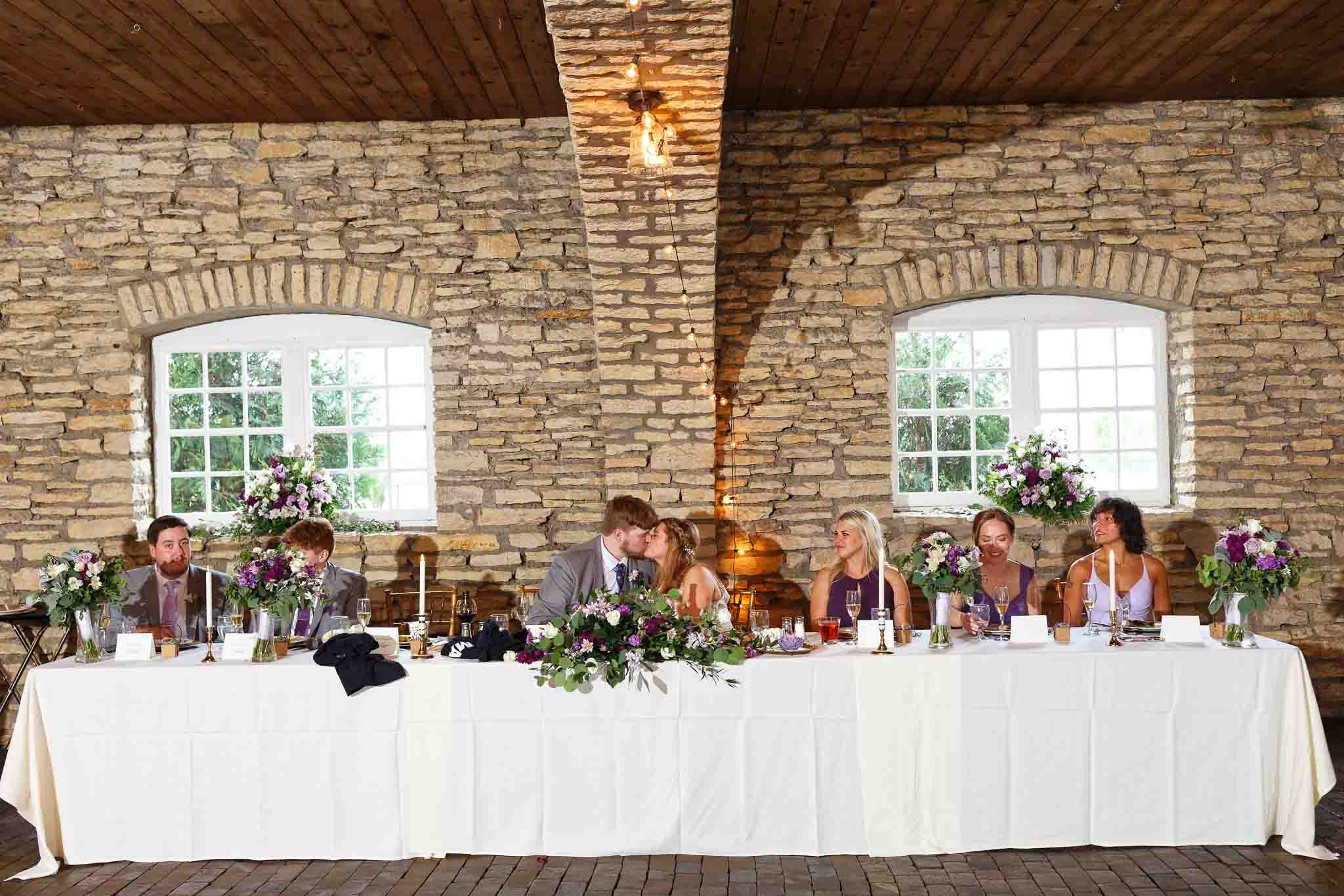 057-bride and groom kissing while guest tapping glass
