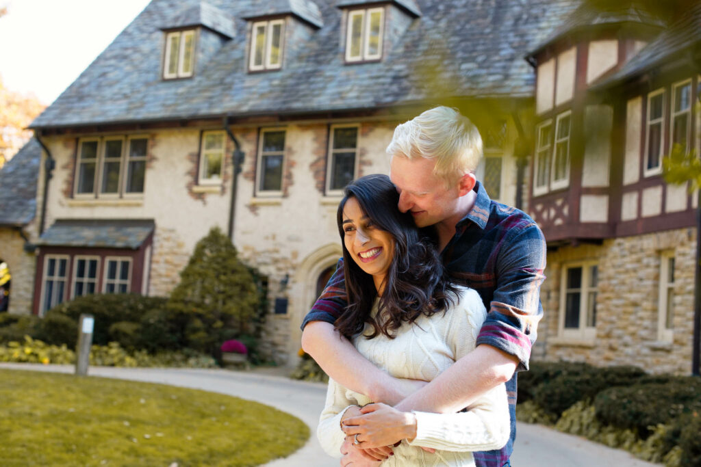Engaged couple in front of the Plummer House Rochester MN, the man is whispering at his fiancé ear