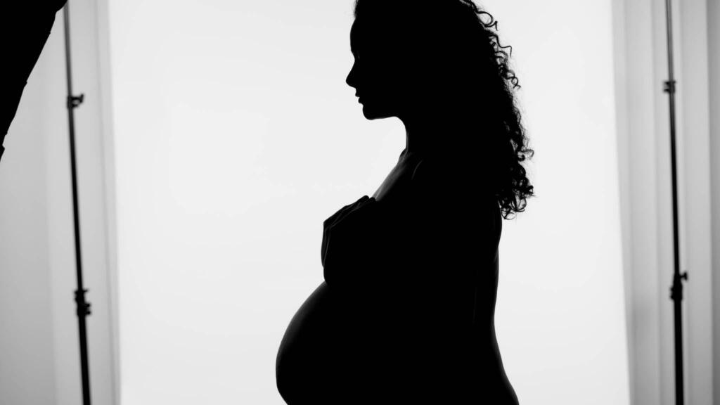 Artistic studio maternity photography in Rochester MN featuring a pregnant woman in a modern silhouette pose against a simple backdrop.