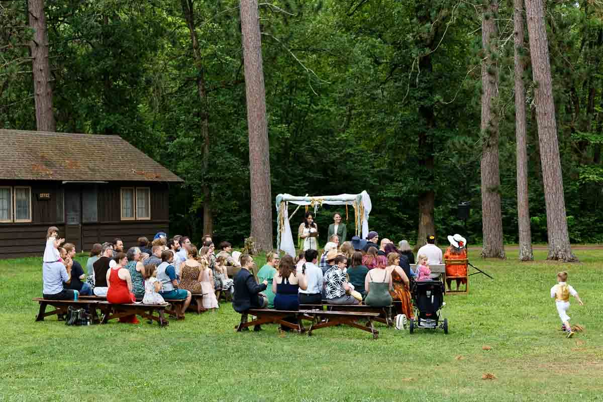 outdoor wedding ceremony under the trees at st. croix state park, minnesota, two brides exchanging vows with guests seated on the lawn