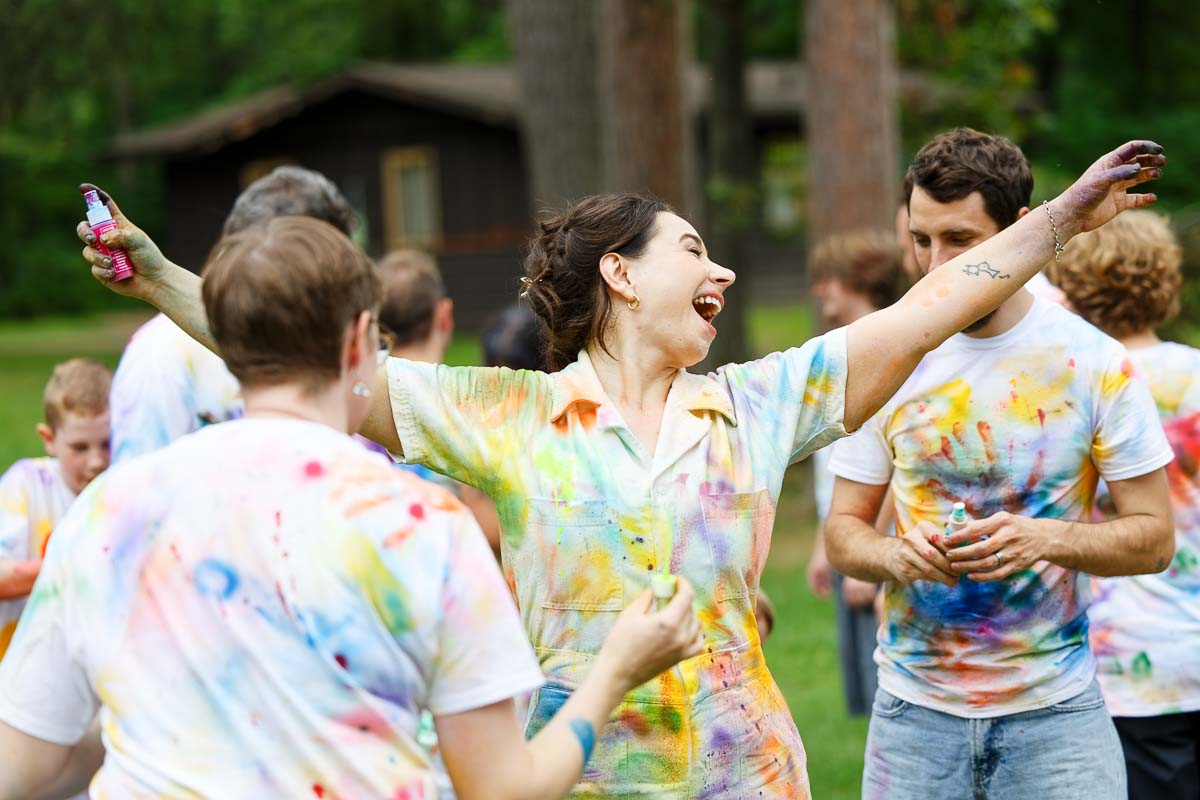 tie-dye activity at outdoor minnesota wedding, kids and adults throwing dye on white t-shirts, colorful candid wedding photography