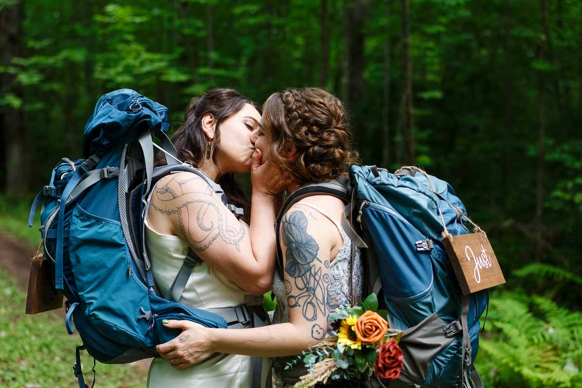 two brides hiking with backpacks and just married sign, outdoor wedding photography in minnesota state park forest trail-2