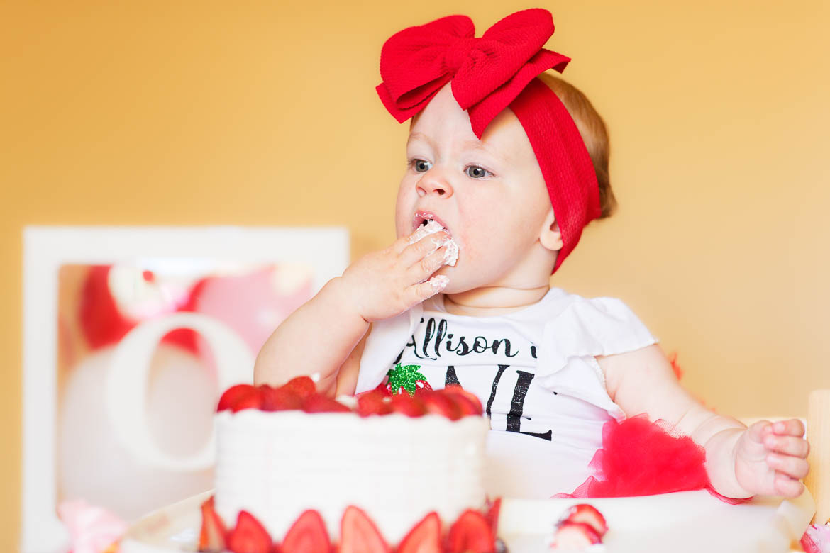 one year old using her fingers to eat birthday cake
