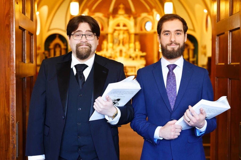 The two ushers at the church entrance holding the wedding ceremony programs