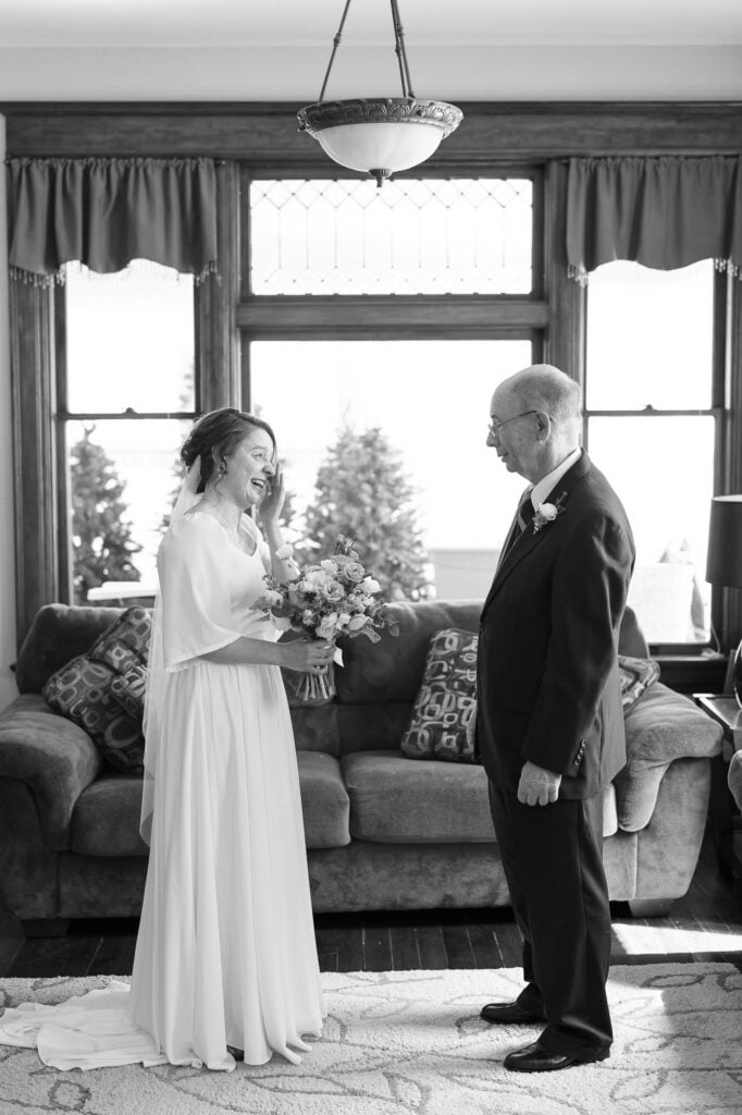Black and white photo of the bride wiping her face after crying during the first look with her father
