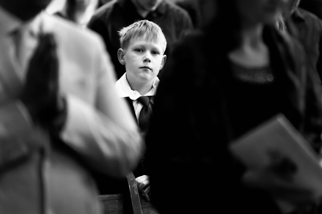 Unposed moment capturing a child lost in thought amid the solemnity of the service