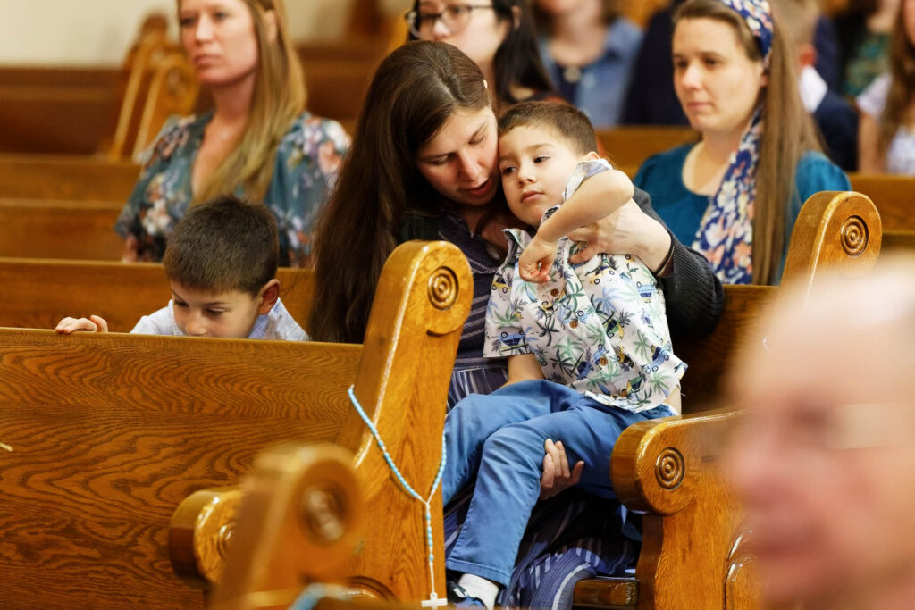 A lighthearted scene as a child gets scolded by his mother during the ceremony, while his brother entertains himself with the church pew