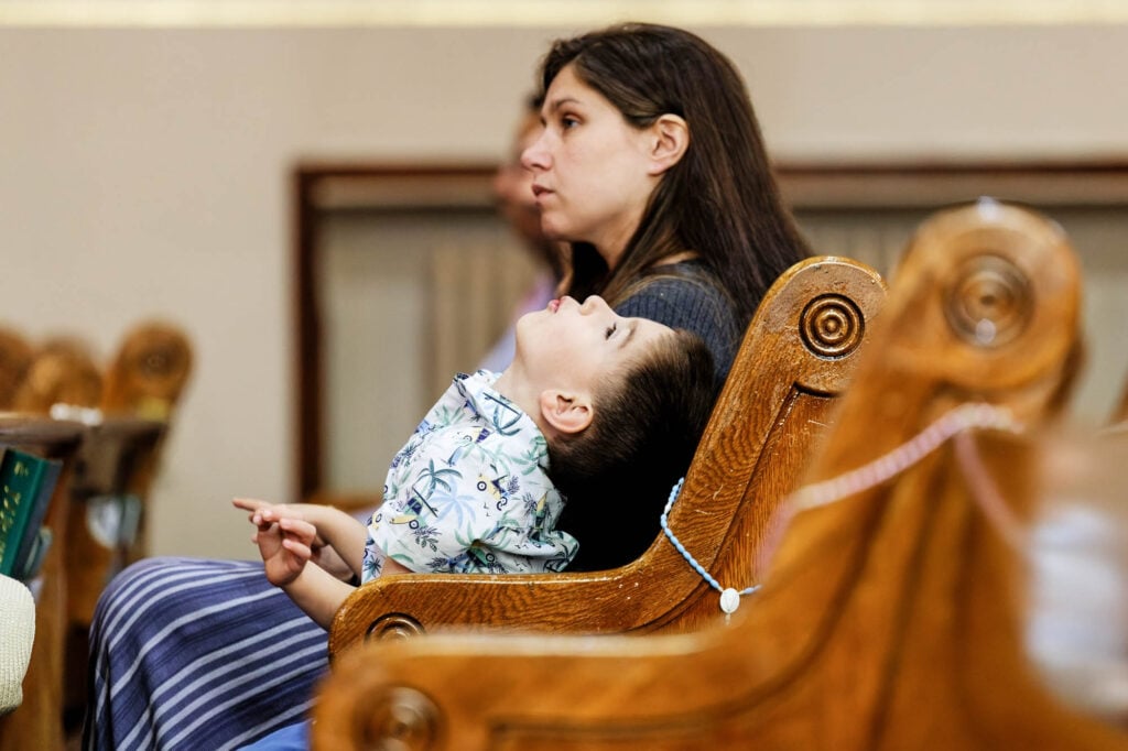 Funny shot of a bored child staring at the ceiling during the church service, right after being scolded by his mom sitting beside him