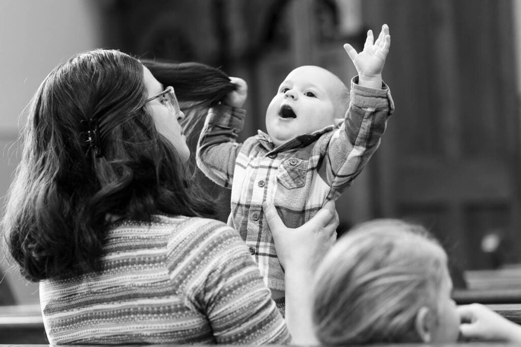 A baby in his mother’s arms at church, tugging her hair and letting out a loud cry
