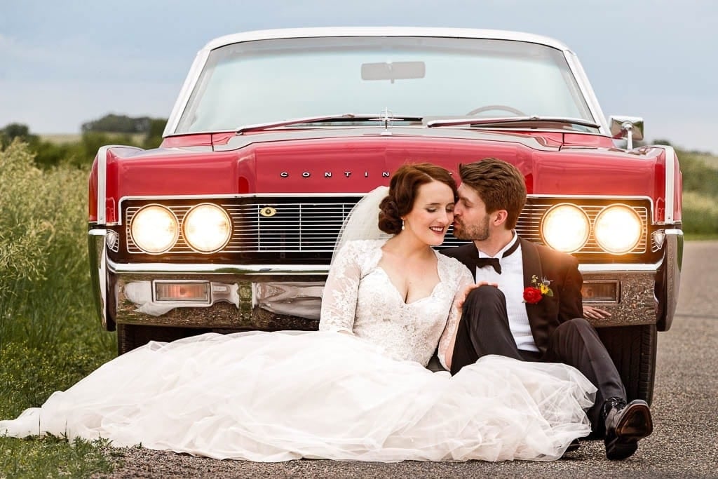 bride and groom sitting with old american read car