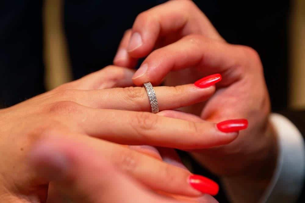 groom puting wedding ring on brides finger with red manicured nails