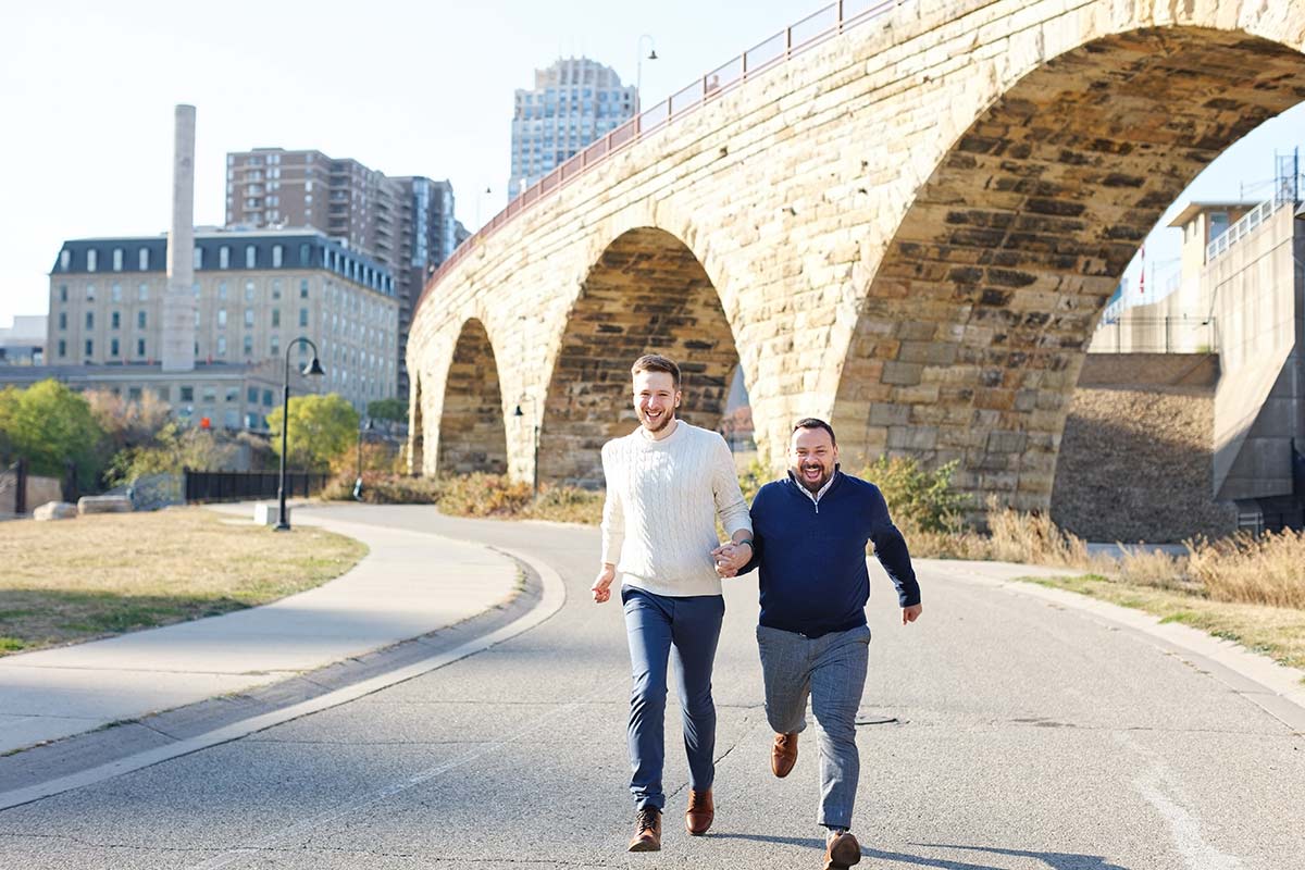 couple-running-during-engagement-session-with-stone-arch-bridge-in-the-back