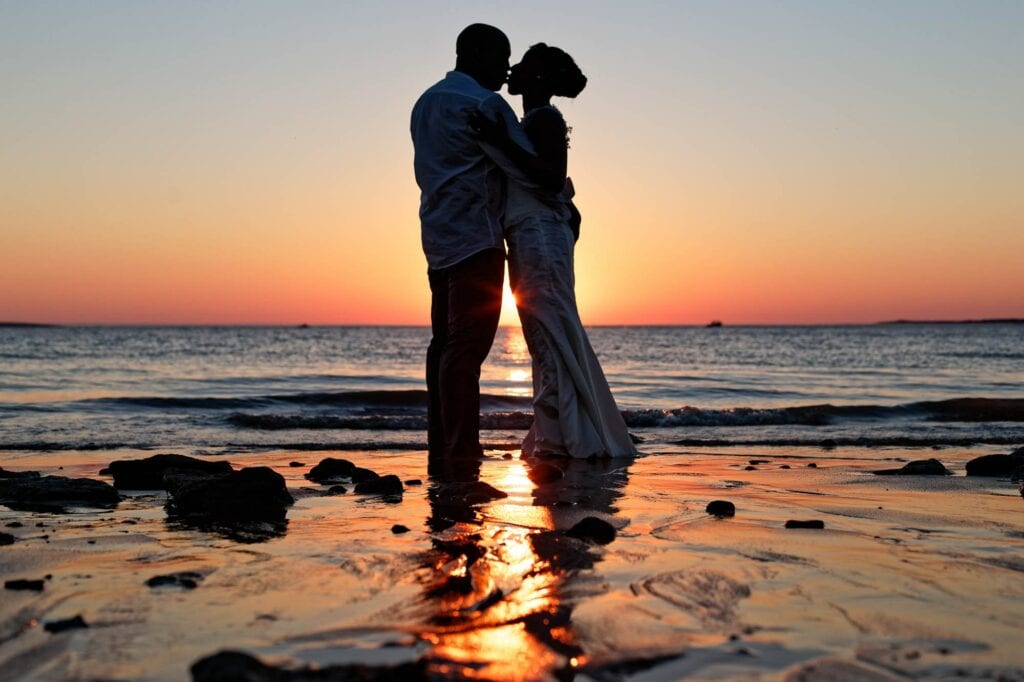 sunset on the beach with bride and groom kissing