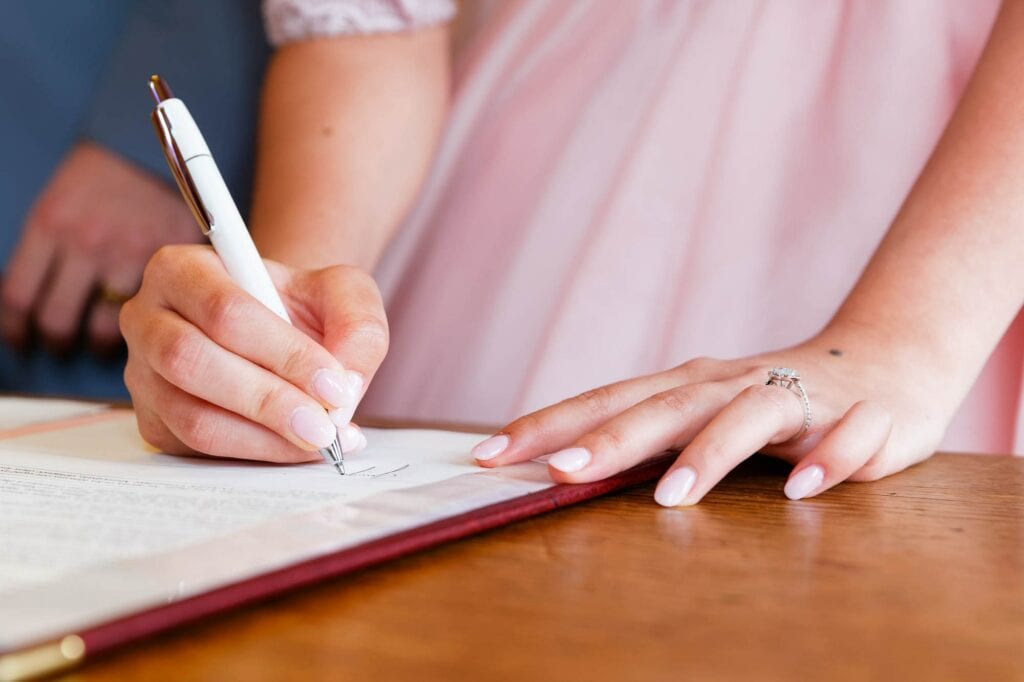 close up of hands signing wedding certificate