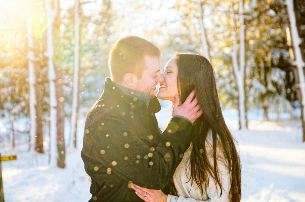 couple kissing during winter with snow sun in backlight