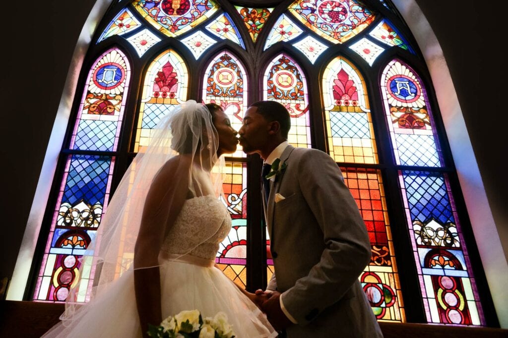 bride and groom kissing in front of church windows