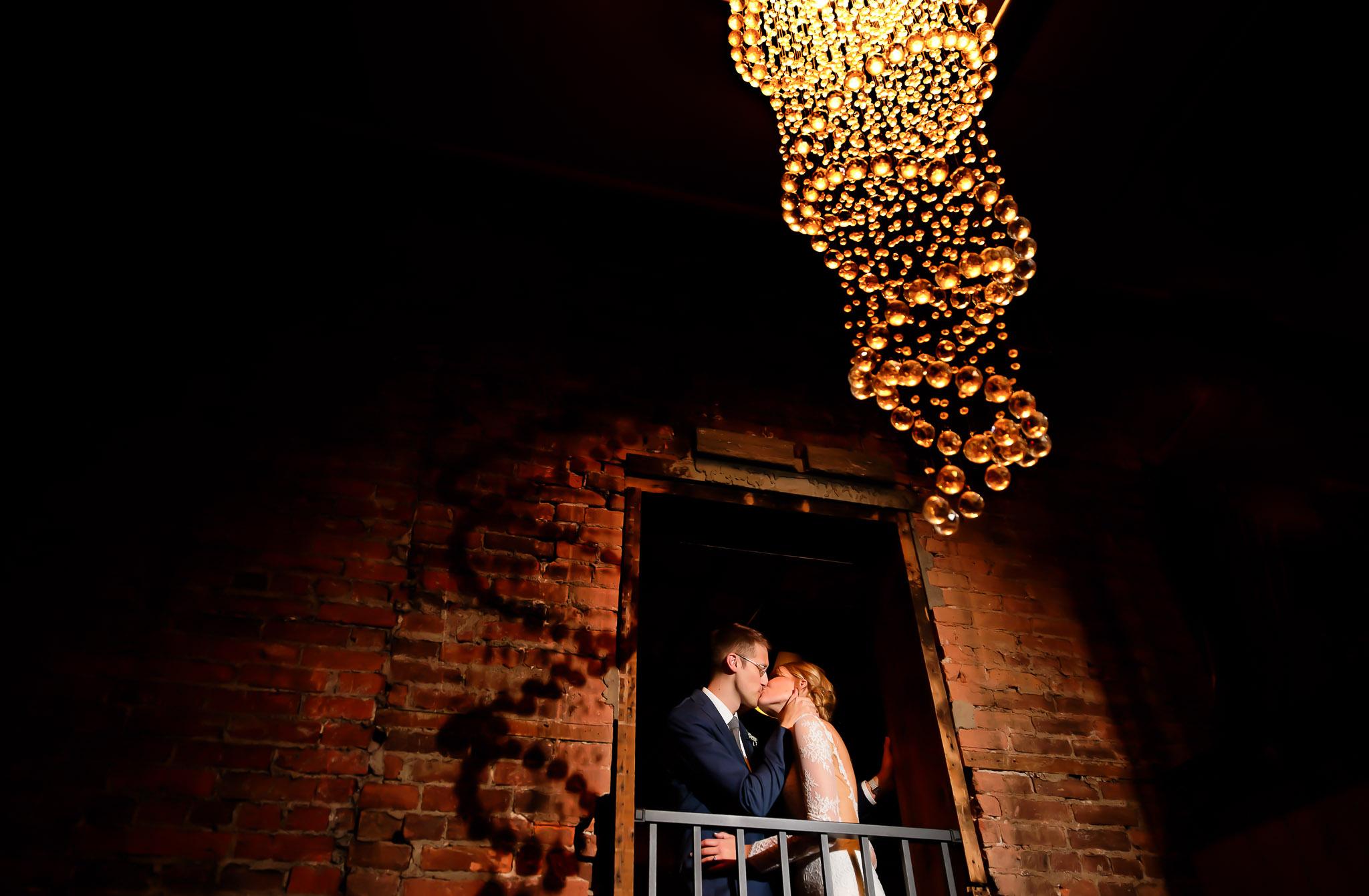 Romantic Wedding Kiss Under Chandelier at Brick Venue
