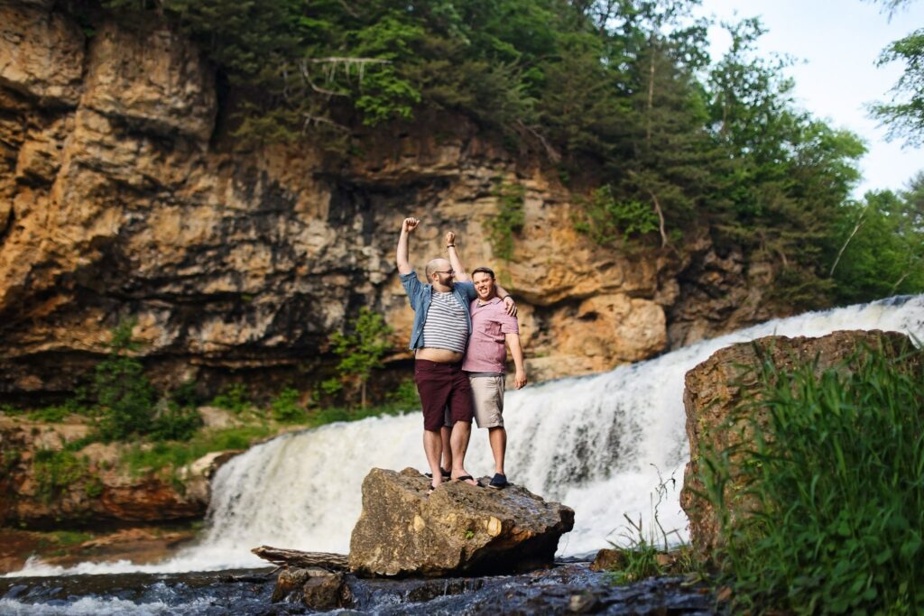 Engagement Photography at Willow River State Park Waterfall: the happy couple raising end in the air
