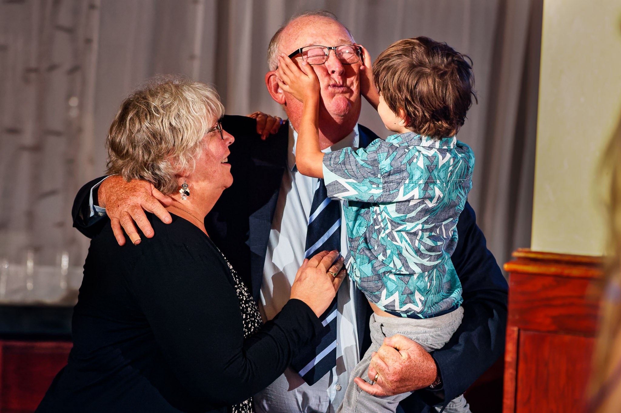 Child Playfully Squeezes Grandpa's Face During Wedding Reception