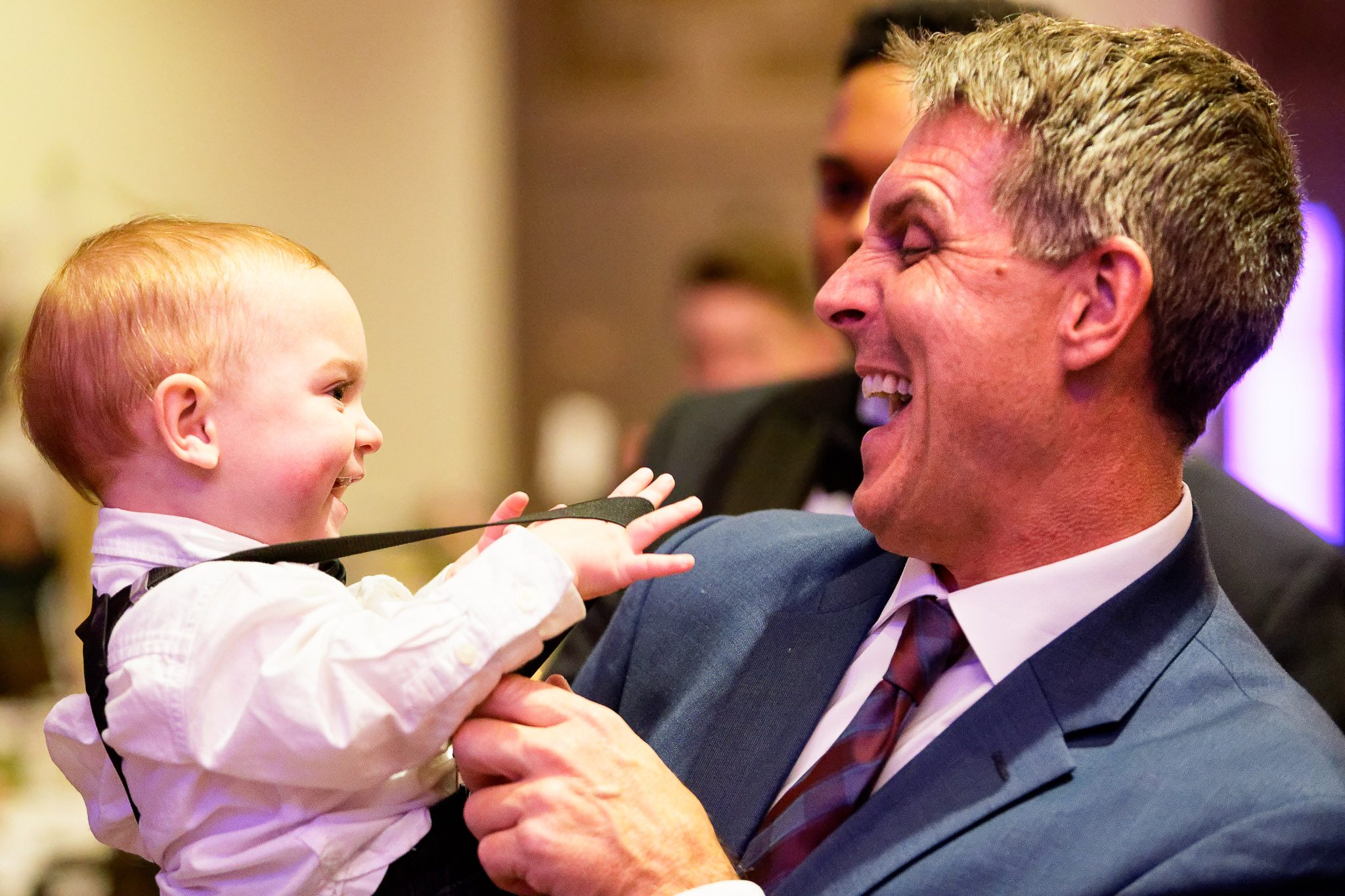 Child Playing with Grandfather's Suspenders at Wedding